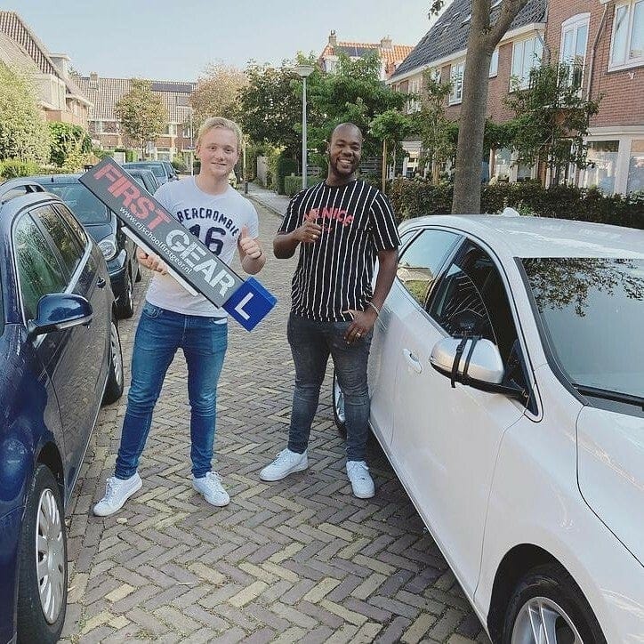 Twee leerlingen met het First Gear-bord bij de lesauto.